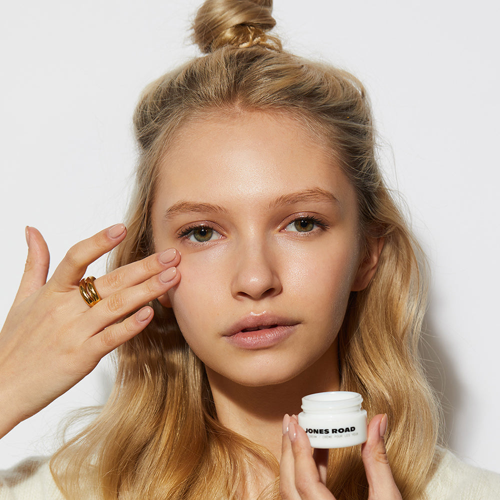 A woman putting on Jones Road Beauty's moisturizing Eye Cream