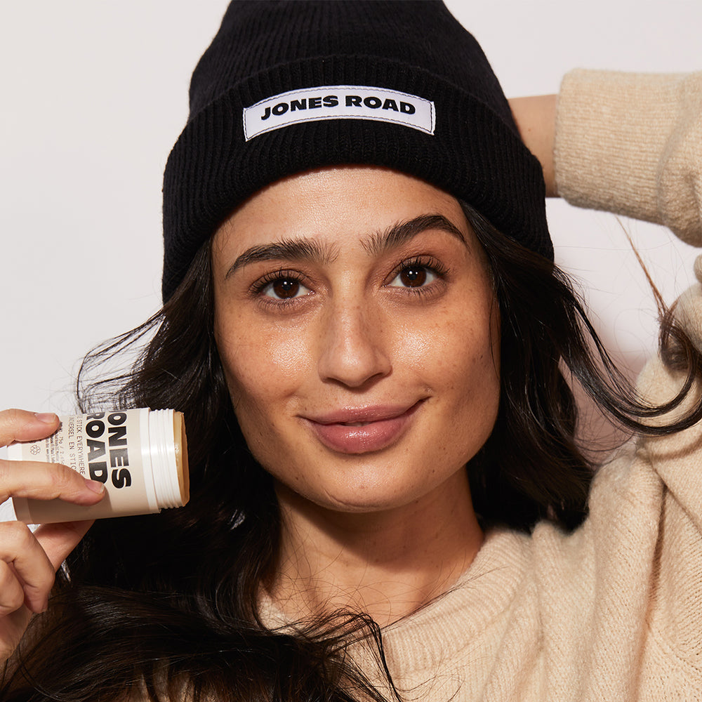 A woman holding The Hippie Stick while wearing Jones Road Beauty's The Beanie