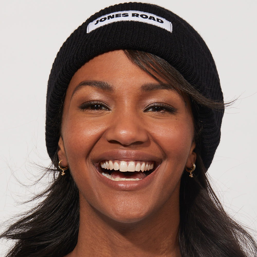 A woman showing off The Beanie with Jones Road Beauty's logo on the front